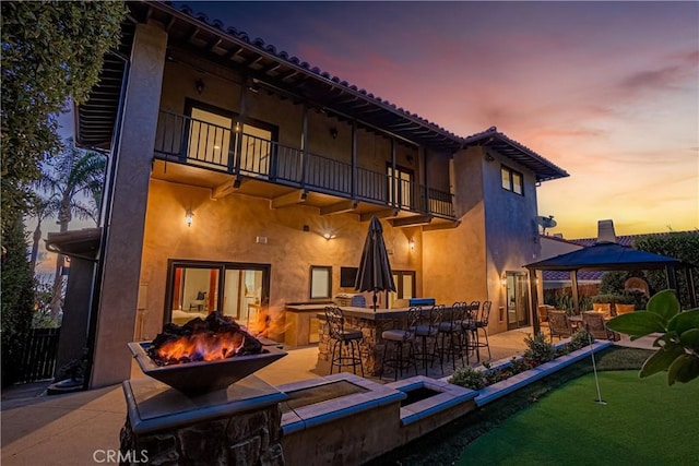 back house at dusk featuring a balcony, a patio area, and exterior bar