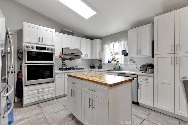 kitchen featuring stainless steel appliances, light tile patterned flooring, vaulted ceiling, white cabinets, and sink