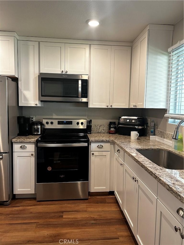 kitchen with dark hardwood / wood-style floors, sink, white cabinetry, light stone countertops, and appliances with stainless steel finishes