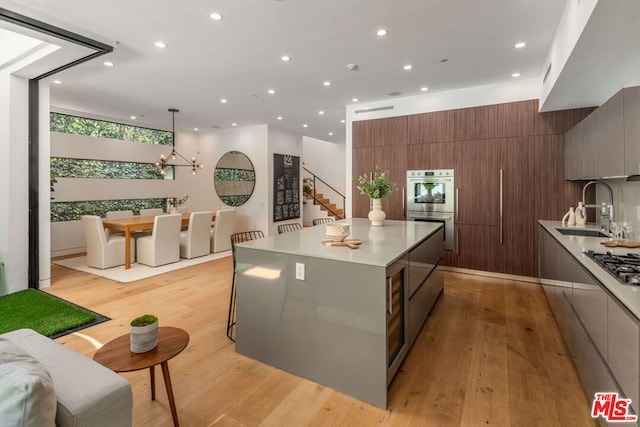 kitchen with light hardwood / wood-style floors, appliances with stainless steel finishes, pendant lighting, a kitchen island, and sink