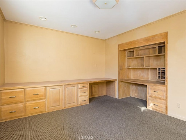 unfurnished office featuring dark colored carpet, built in desk, and crown molding