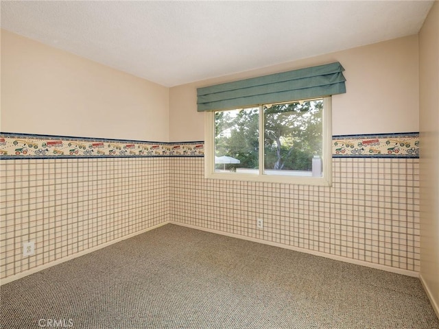 carpeted spare room with tile walls