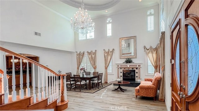 living area featuring an inviting chandelier, a high ceiling, a raised ceiling, crown molding, and light wood-type flooring