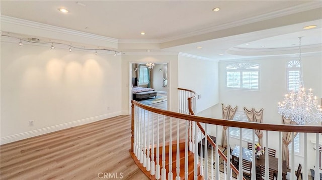 hallway featuring a raised ceiling, ornamental molding, hardwood / wood-style floors, and a notable chandelier