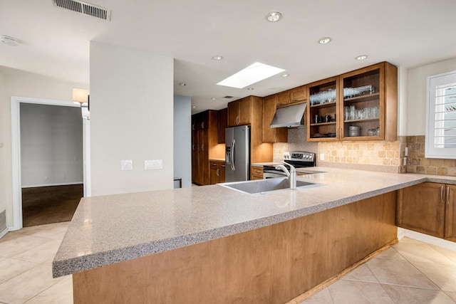 kitchen with kitchen peninsula, sink, a skylight, appliances with stainless steel finishes, and light tile patterned floors