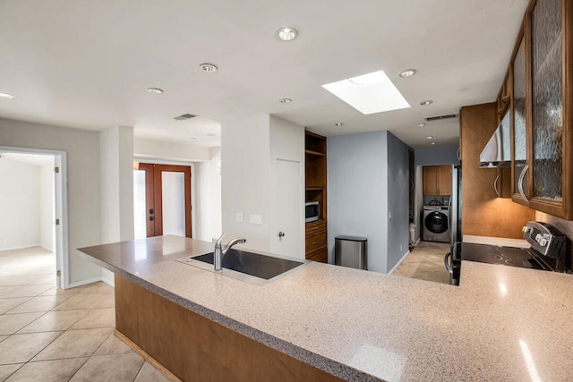 kitchen featuring washer / dryer, a skylight, kitchen peninsula, stainless steel appliances, and sink