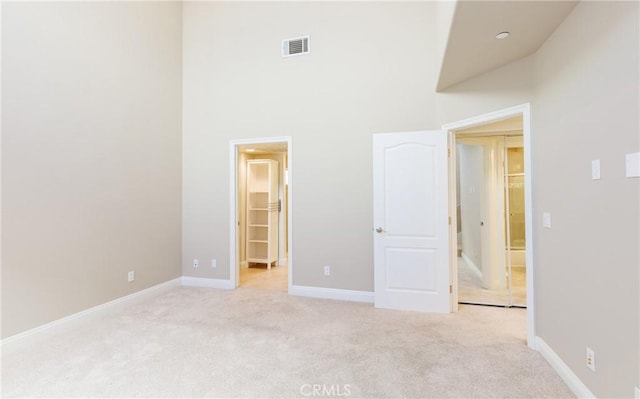 unfurnished bedroom featuring a high ceiling, a walk in closet, a closet, and light colored carpet