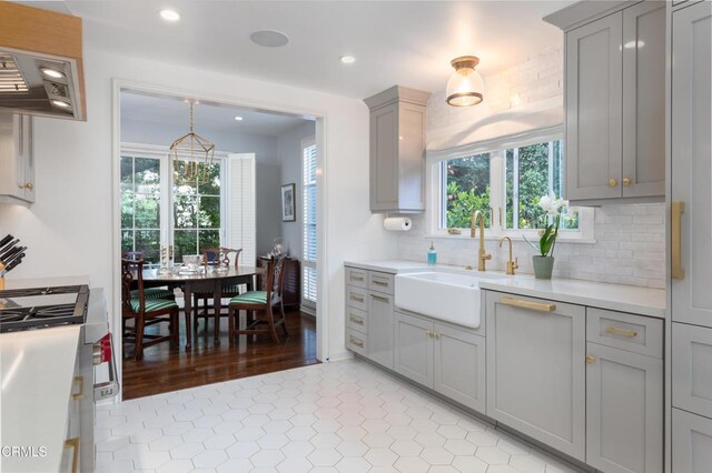 kitchen featuring light tile patterned floors, gray cabinets, decorative backsplash, decorative light fixtures, and sink