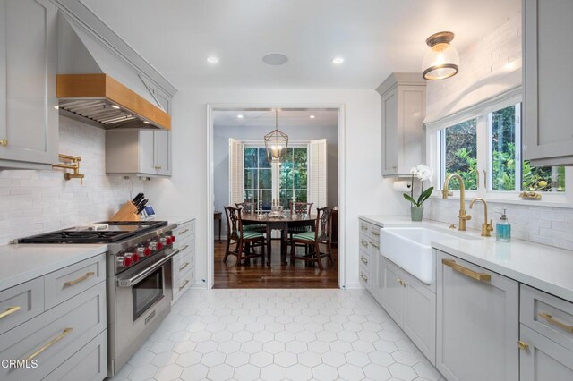 kitchen featuring pendant lighting, decorative backsplash, designer range, sink, and gray cabinets