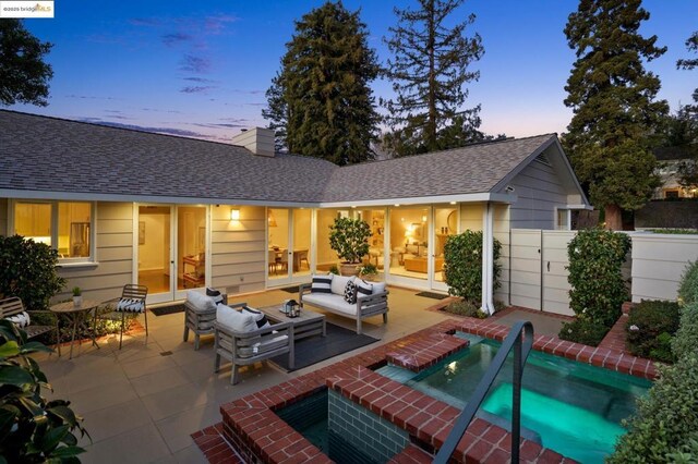 back house at dusk with outdoor lounge area, a jacuzzi, and a patio