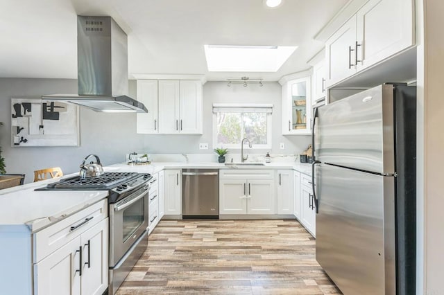 kitchen featuring white cabinetry, wall chimney range hood, a skylight, stainless steel appliances, and sink