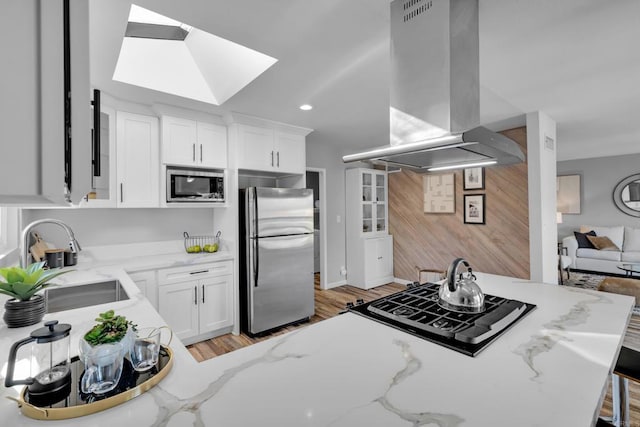 kitchen with island range hood, light stone countertops, white cabinetry, and appliances with stainless steel finishes