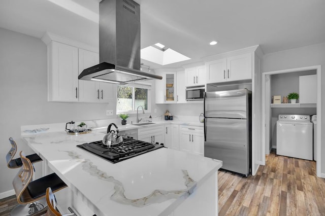 kitchen with white cabinetry, a skylight, island exhaust hood, stainless steel appliances, and sink