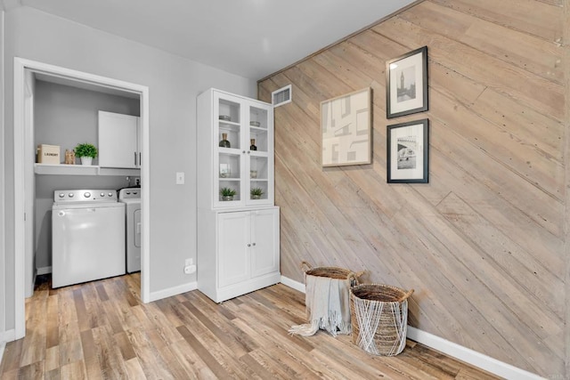 laundry area with wood walls, cabinets, light hardwood / wood-style flooring, and washing machine and clothes dryer