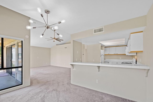 kitchen featuring light colored carpet, vaulted ceiling, kitchen peninsula, white cabinetry, and a kitchen breakfast bar