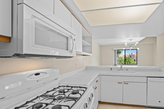 kitchen with kitchen peninsula, a notable chandelier, white appliances, white cabinets, and sink