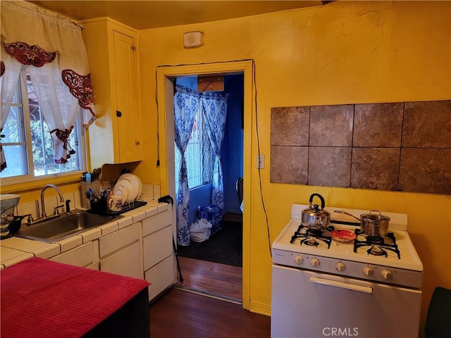 kitchen featuring white range with gas stovetop, white cabinets, sink, and tile countertops