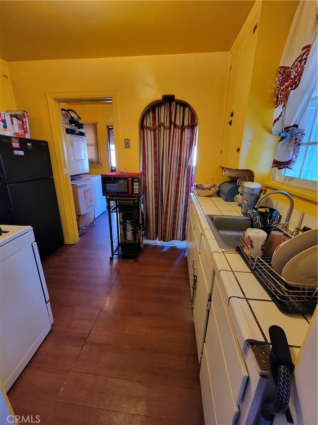 kitchen with black refrigerator, white cabinetry, separate washer and dryer, white range oven, and tile counters