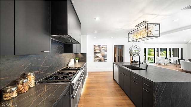 kitchen featuring dishwasher, wall chimney exhaust hood, sink, hanging light fixtures, and light hardwood / wood-style flooring