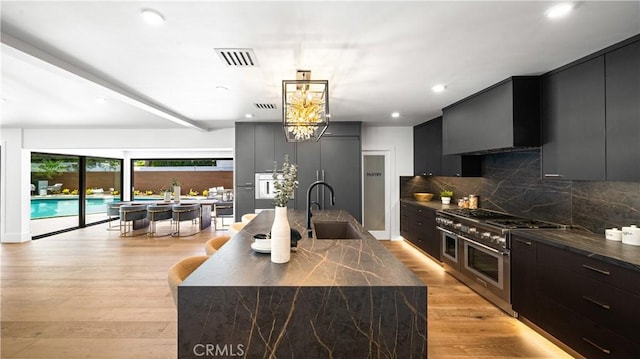 kitchen featuring tasteful backsplash, light hardwood / wood-style floors, double oven range, sink, and an island with sink