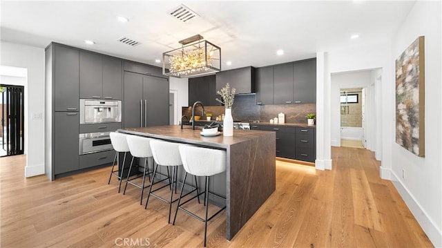 kitchen featuring an island with sink, decorative backsplash, light wood-type flooring, a kitchen breakfast bar, and hanging light fixtures