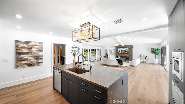 kitchen with dishwasher, vaulted ceiling with beams, a large fireplace, sink, and a kitchen island with sink