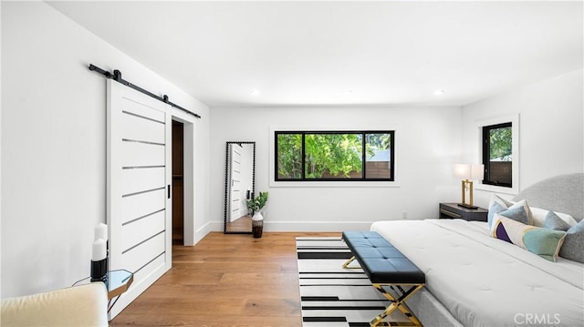 bedroom with a barn door, light hardwood / wood-style flooring, and multiple windows