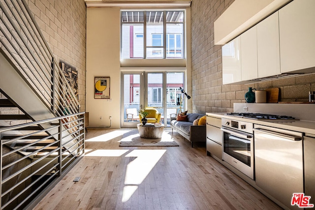 kitchen featuring white cabinets, a high ceiling, stainless steel appliances, and light hardwood / wood-style floors