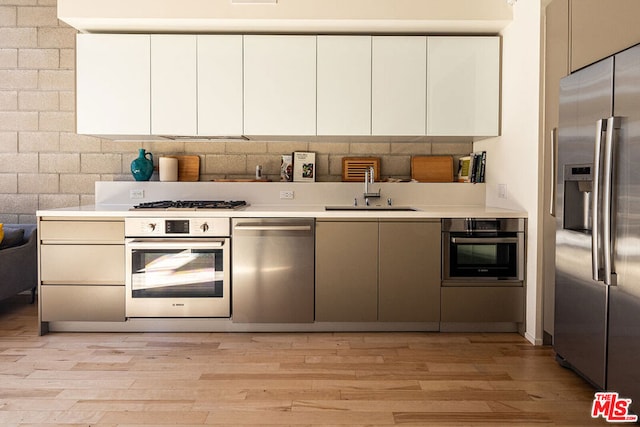 kitchen with stainless steel appliances, light hardwood / wood-style floors, white cabinets, and sink