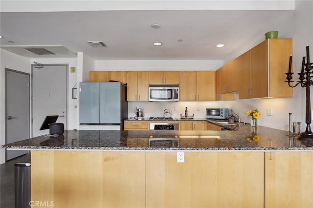 kitchen featuring sink, kitchen peninsula, stainless steel appliances, and dark stone countertops