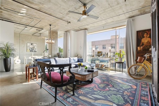 sitting room featuring ceiling fan with notable chandelier and concrete flooring