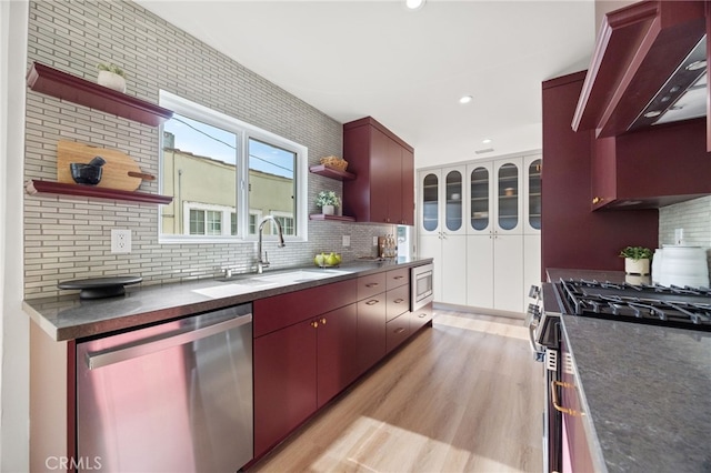 kitchen with custom exhaust hood, sink, decorative backsplash, light wood-type flooring, and stainless steel appliances