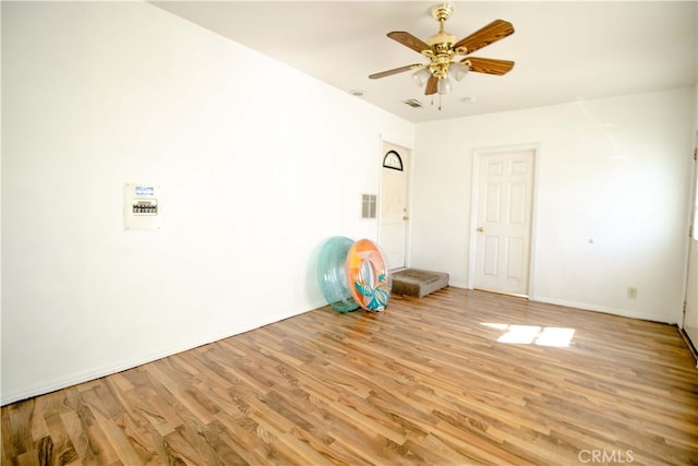 exercise room featuring baseboards, light wood-type flooring, visible vents, and a ceiling fan