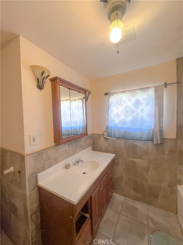 bathroom with a wainscoted wall, tile patterned flooring, tile walls, and vanity