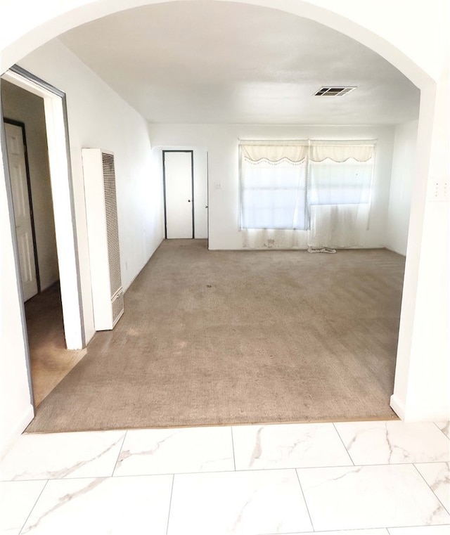 spare room featuring arched walkways, marble finish floor, visible vents, light carpet, and a heating unit