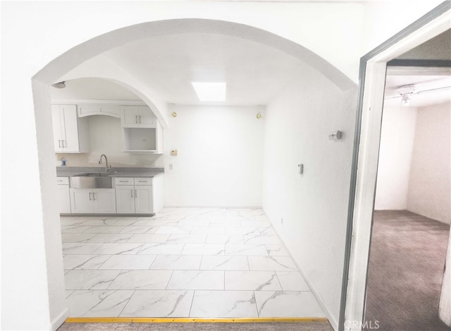 kitchen featuring marble finish floor, light countertops, a sink, and white cabinetry