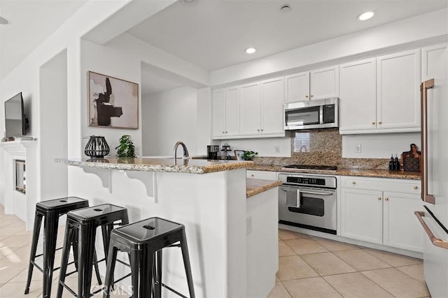 kitchen with white cabinetry, kitchen peninsula, appliances with stainless steel finishes, a kitchen breakfast bar, and light stone counters