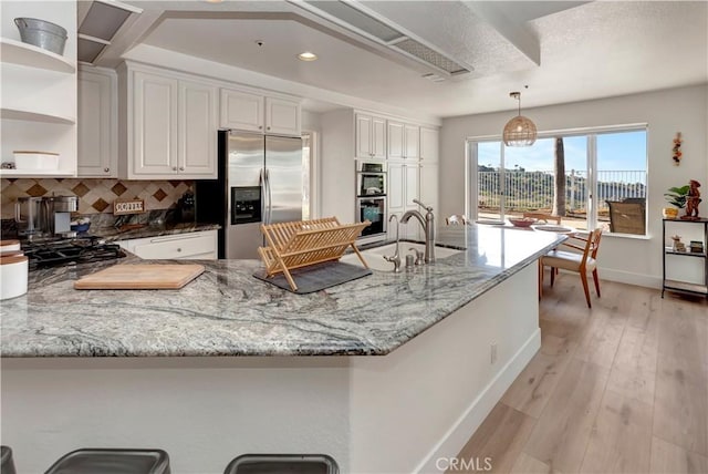 kitchen featuring light stone countertops, white cabinetry, stainless steel fridge, and hanging light fixtures