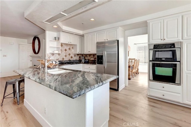 kitchen with white cabinets, appliances with stainless steel finishes, decorative backsplash, sink, and light hardwood / wood-style floors