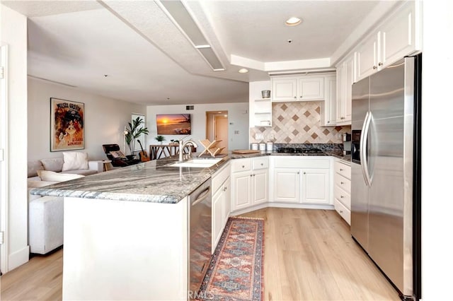 kitchen with white cabinetry, kitchen peninsula, appliances with stainless steel finishes, stone countertops, and sink