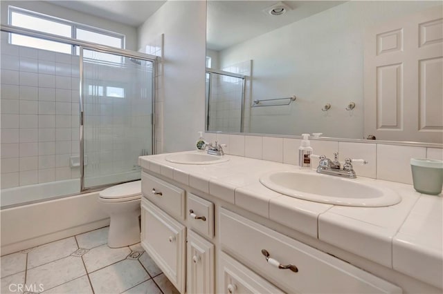 full bathroom featuring toilet, backsplash, tile patterned floors, vanity, and shower / bath combination with glass door