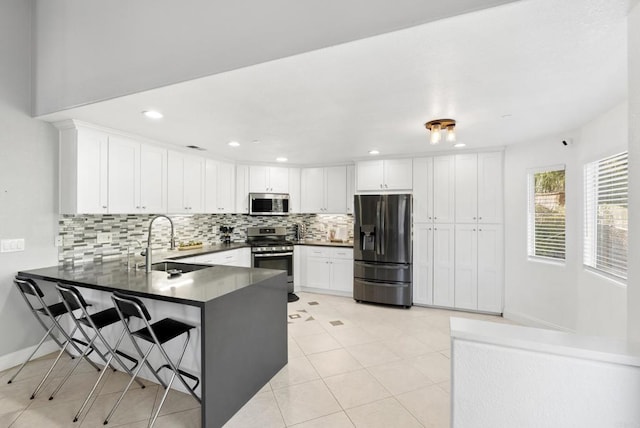 kitchen with kitchen peninsula, a kitchen bar, sink, white cabinetry, and appliances with stainless steel finishes