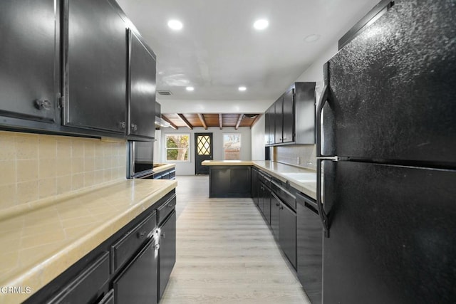 kitchen with black refrigerator, light wood-type flooring, stainless steel dishwasher, and tasteful backsplash