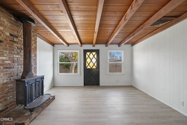 interior space featuring wood ceiling, light hardwood / wood-style floors, wooden walls, a wood stove, and beamed ceiling