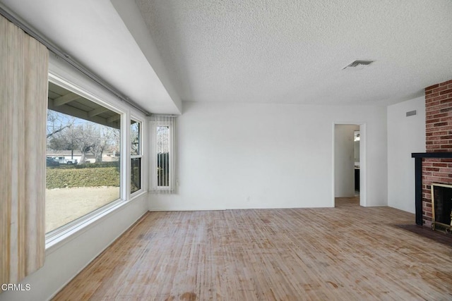 unfurnished living room featuring light wood-type flooring, a brick fireplace, and a textured ceiling