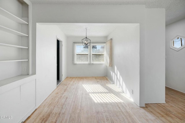 unfurnished dining area with light hardwood / wood-style floors, a textured ceiling, built in features, and an inviting chandelier