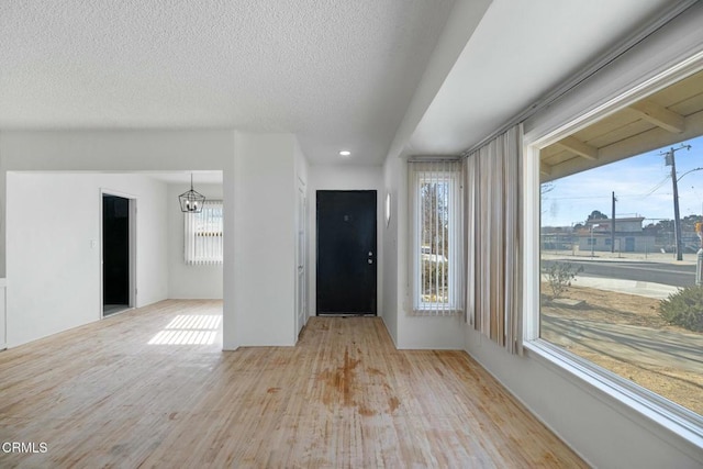 foyer entrance with a healthy amount of sunlight, light wood-type flooring, a chandelier, and a textured ceiling