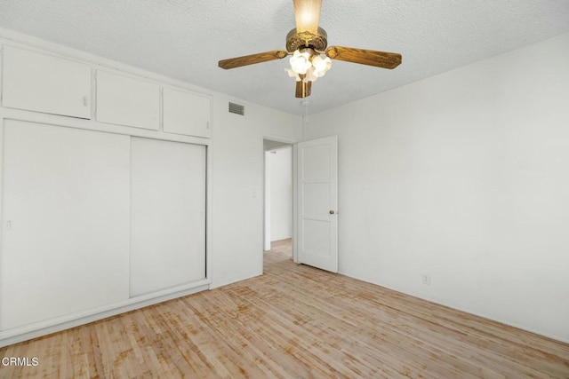 unfurnished bedroom featuring ceiling fan, a textured ceiling, a closet, and light wood-type flooring