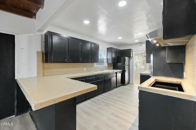 kitchen featuring beamed ceiling, tasteful backsplash, black fridge, kitchen peninsula, and light wood-type flooring