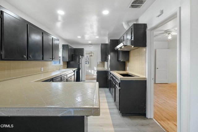 kitchen featuring black appliances, exhaust hood, decorative backsplash, ceiling fan, and light hardwood / wood-style flooring